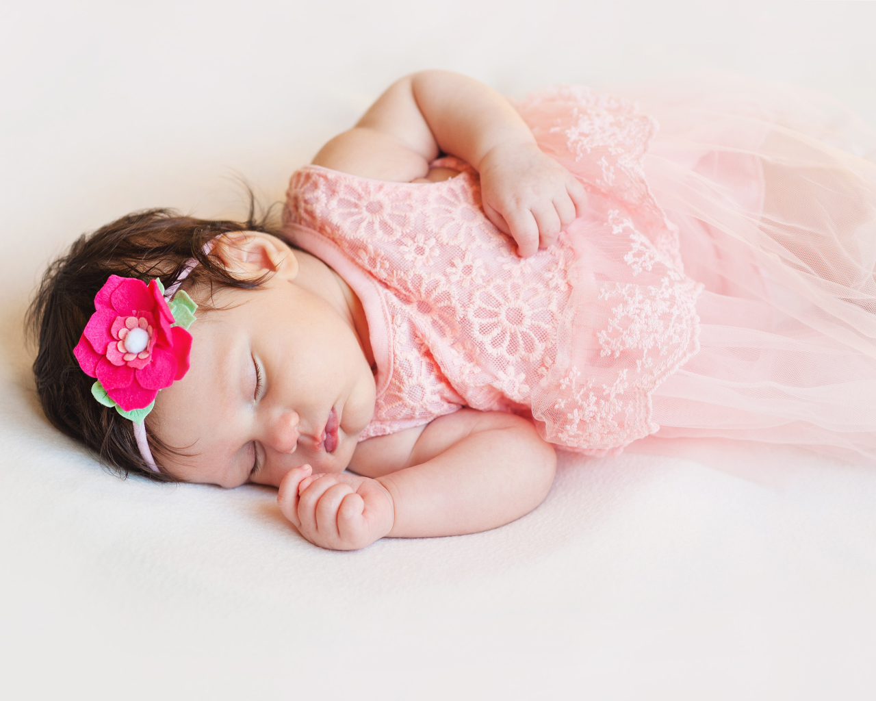 Маленькая спящая девочка в розовом платье с цветком в волосах 