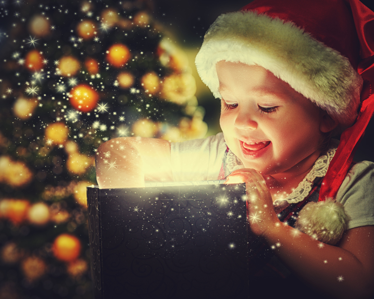 Маленькая улыбающаяся девочка открывает подарок у новогодней елки 