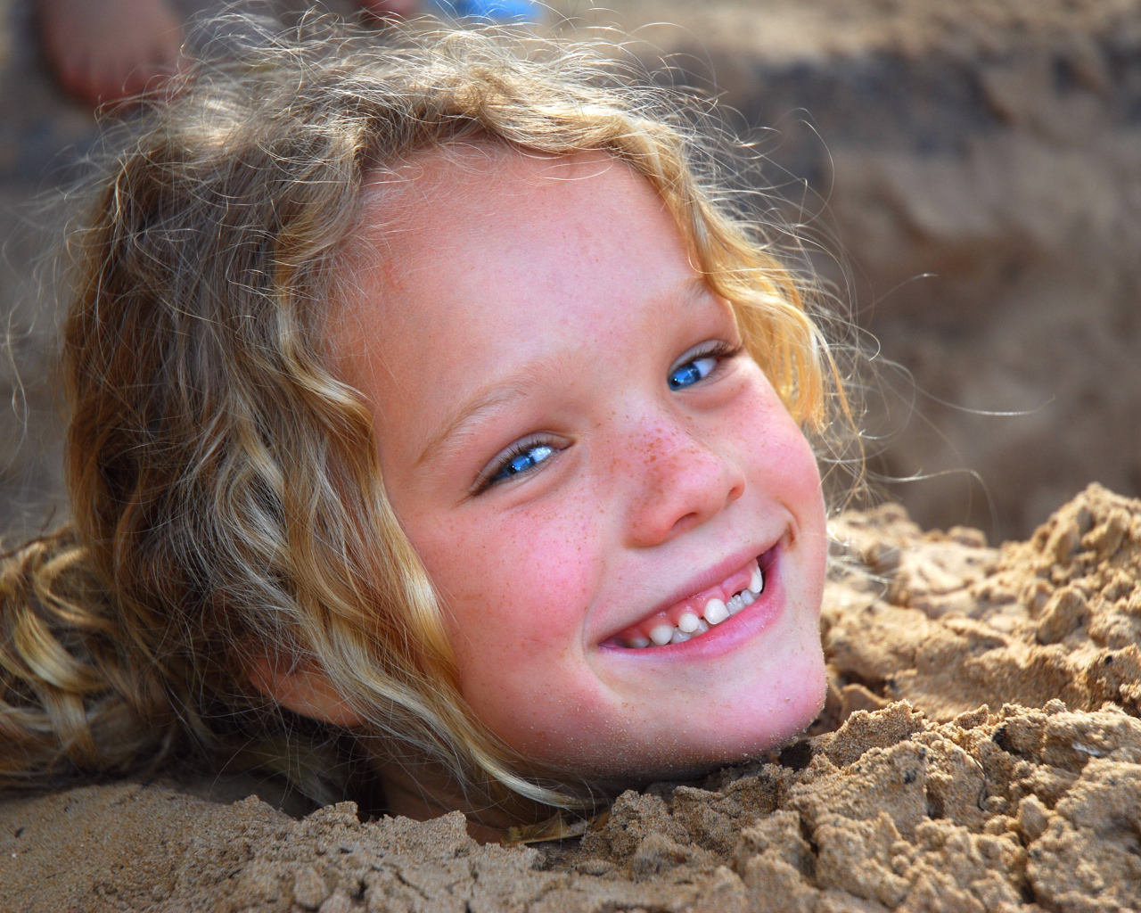 Маленькая улыбающаяся девочка играет в песке