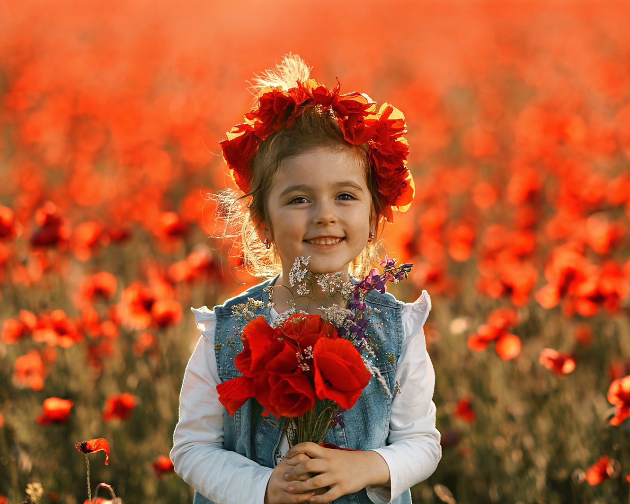 Маленькая улыбающаяся девочка с венком из красных маков на голове и букетом в руках
