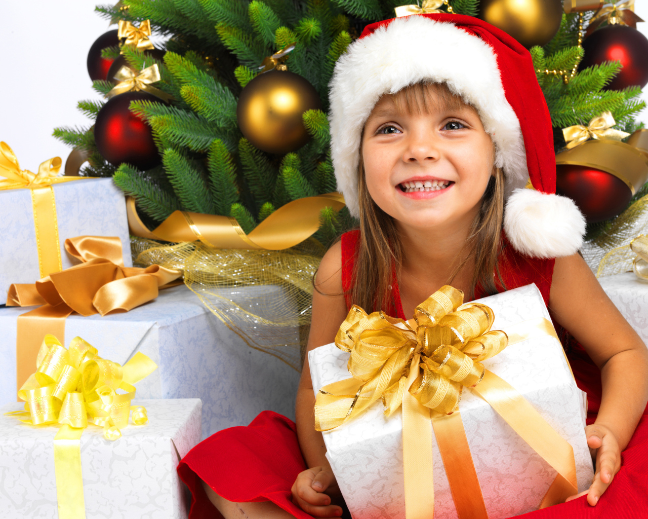 Улыбающаяся девочка в новогоднем костюме с подарками под елкой