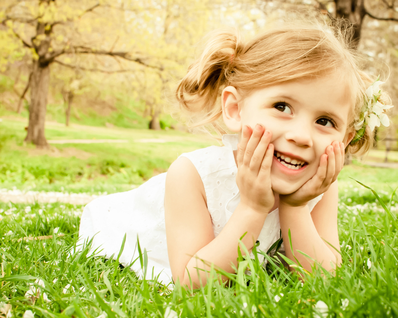 Улыбающаяся девочка в белом платье лежит на зеленой траве
