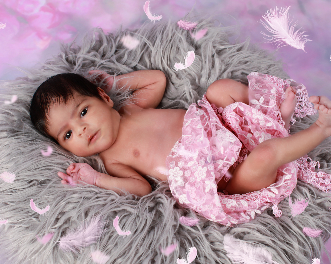 Младенец лежит на сером меховом покрывале 
