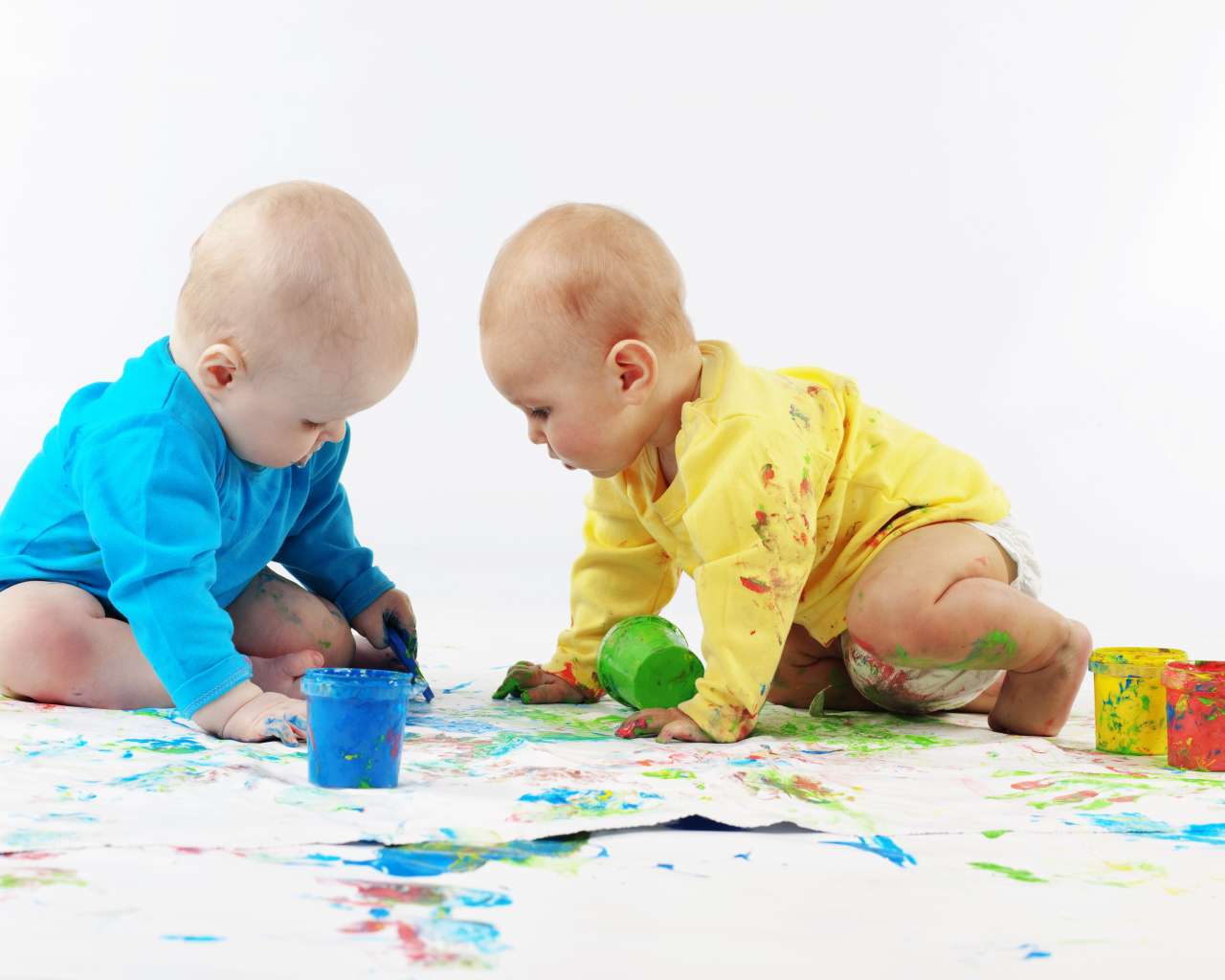 Два малыша рисуют красками на белом фоне