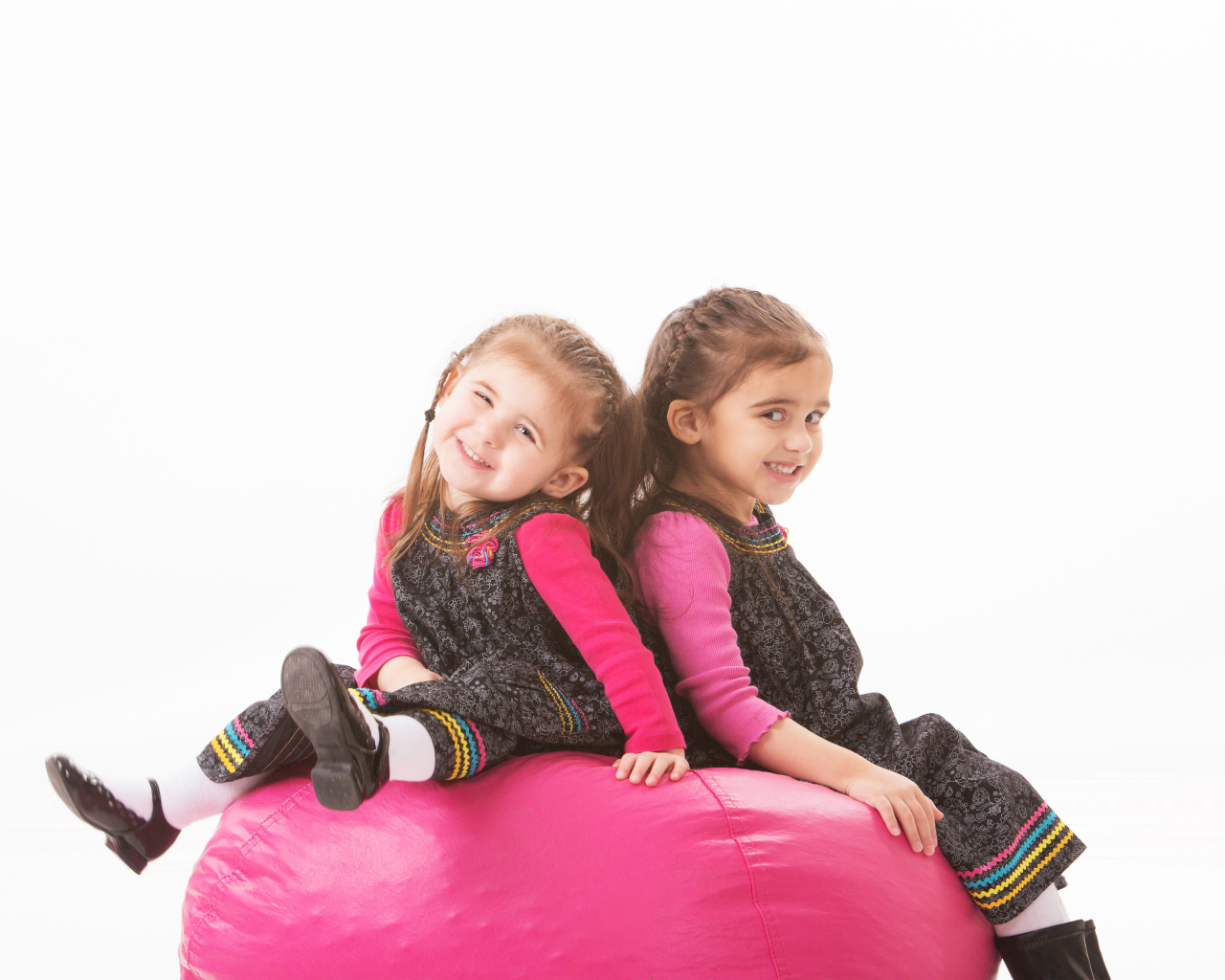 Две маленькие девочки сидят на красном мягком шаре 