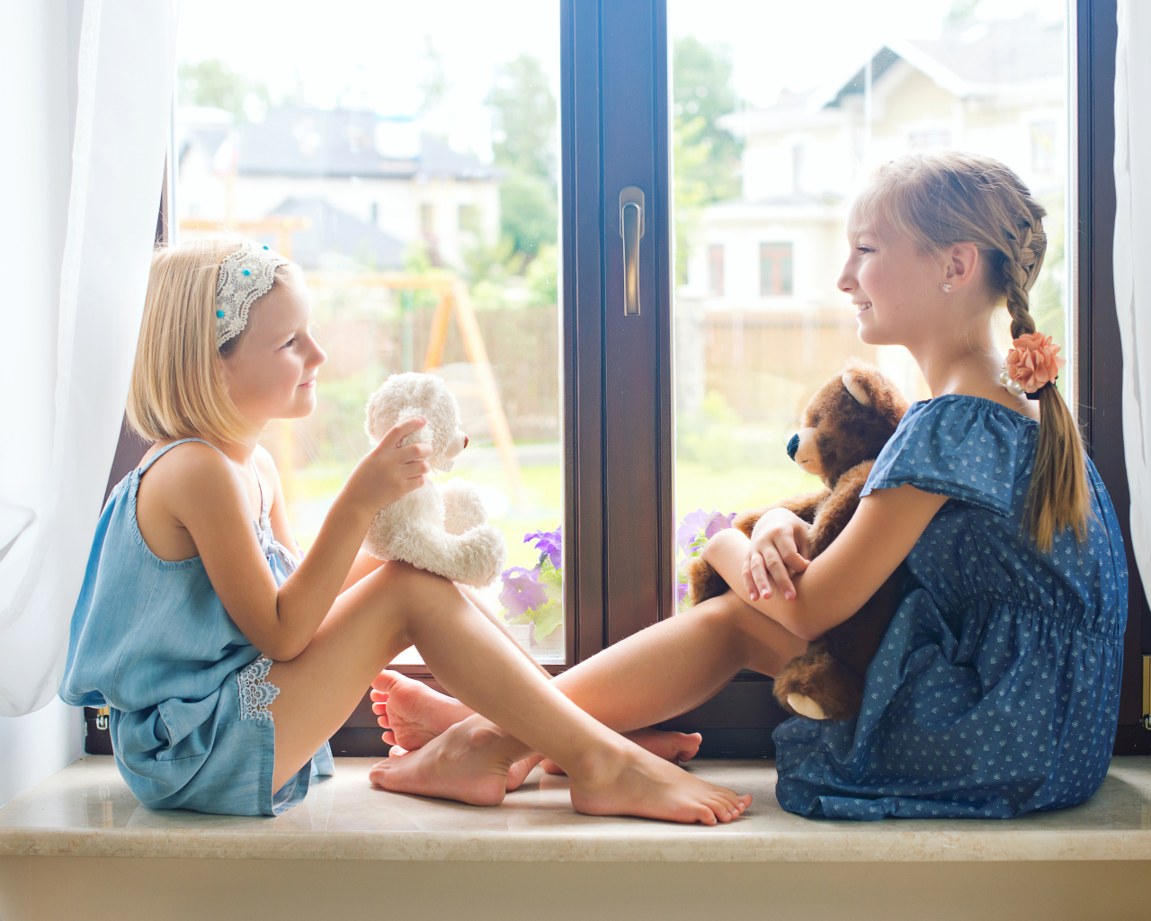 Две маленькие девочки с игрушками сидят на подоконнике у окна