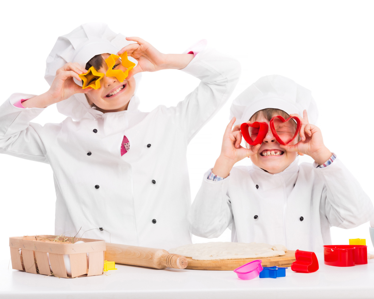 Два маленьких ребенка в костюмах повара готовят на кухне печенье