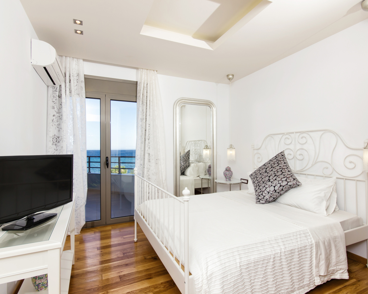 Светлая спальня с большой белой кроватью и телевизором 