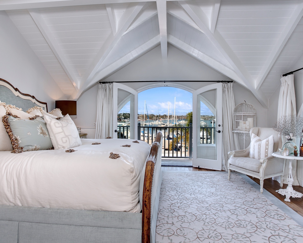 Белая спальня с большой высокой кроватью и балконом 