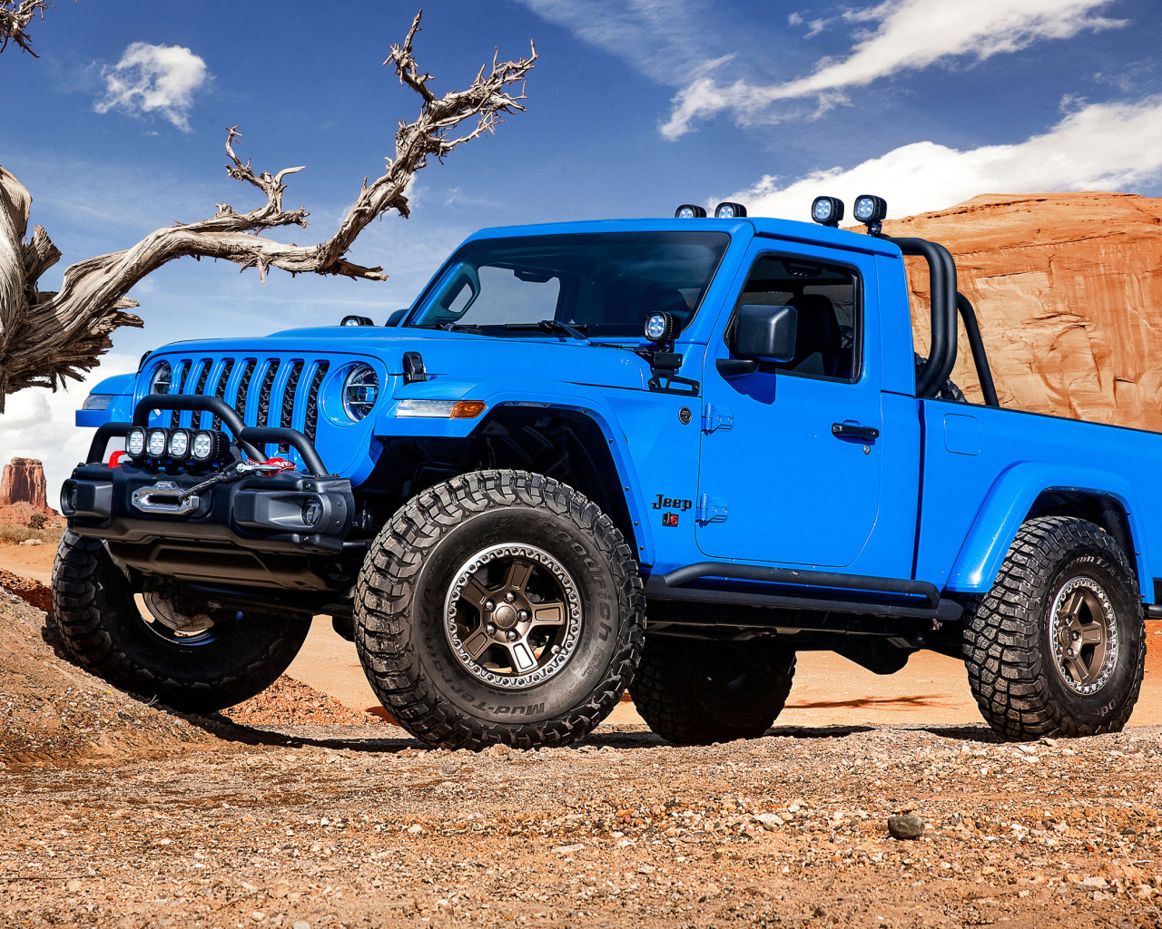 Синий пикап Jeep J6, 2019 года на фоне гор у сухого дерева