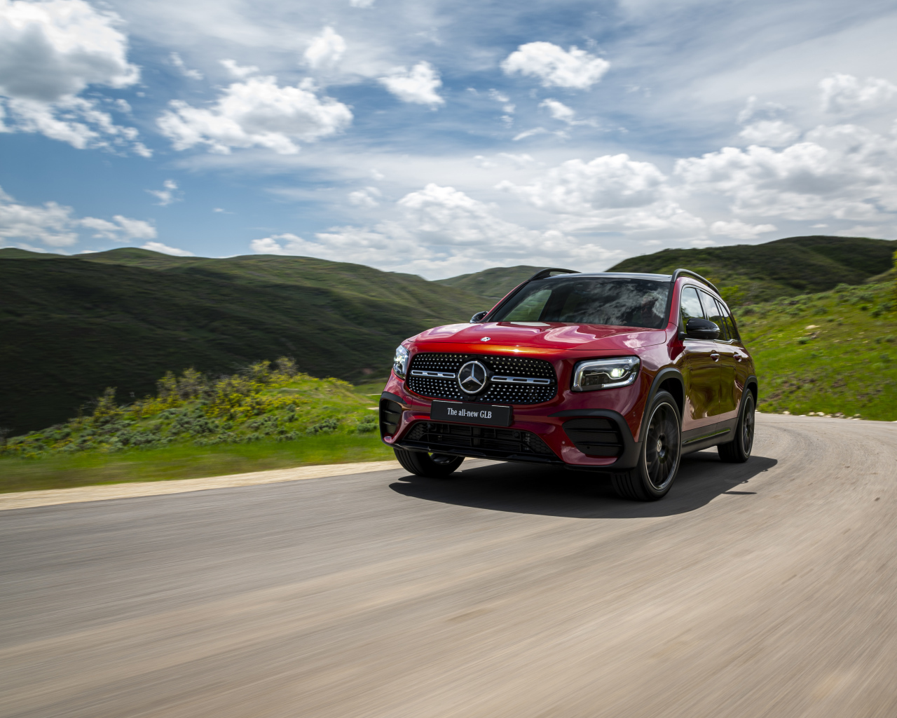 Красный автомобиль Mercedes-Benz GLB-Class  на фоне зеленых холмов