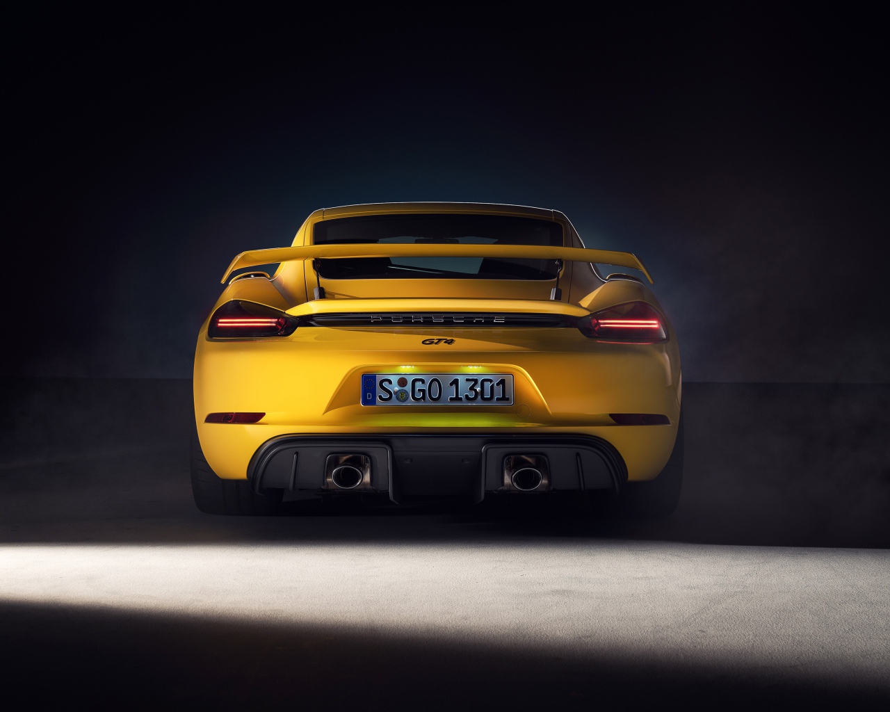 Желтый автомобиль Porsche 718 Cayman GT4, 2019 года вид сзади на сером фоне