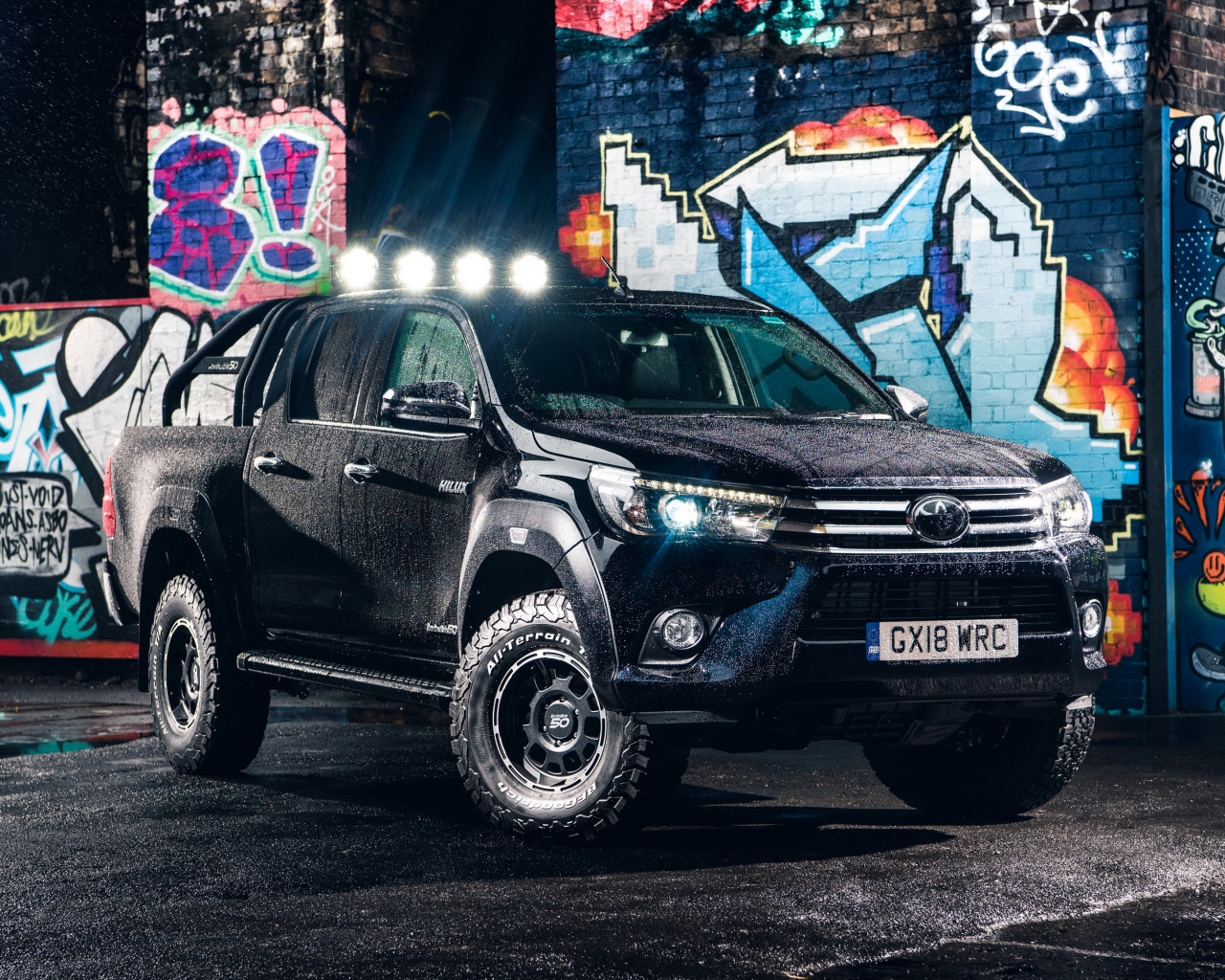 Черный внедорожник Toyota Hilux  под дождем на фоне разрисованной стены