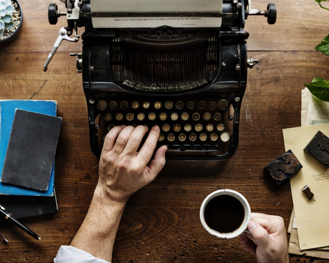 Мужчина с чашкой кофе в руке печатает на старой печатной машинке 