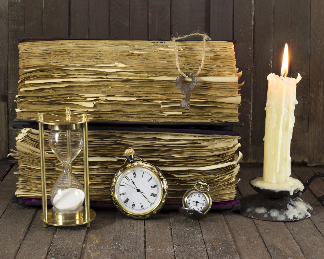 Старинные книги, зажженная свеча, ключи и часы на столе