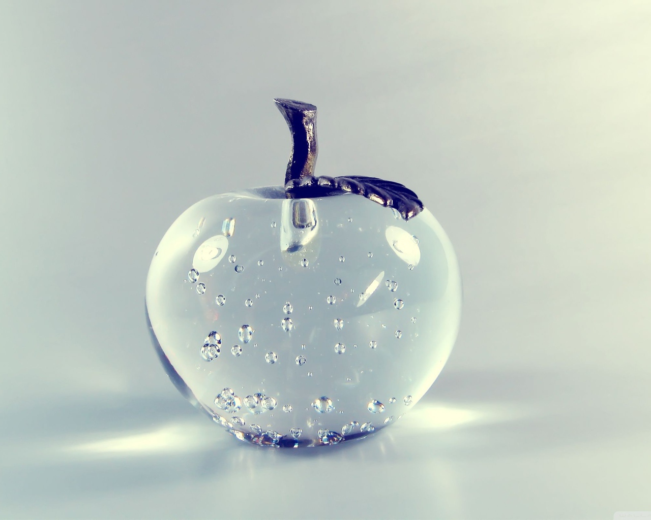 Стеклянное яблоко на сером фоне 