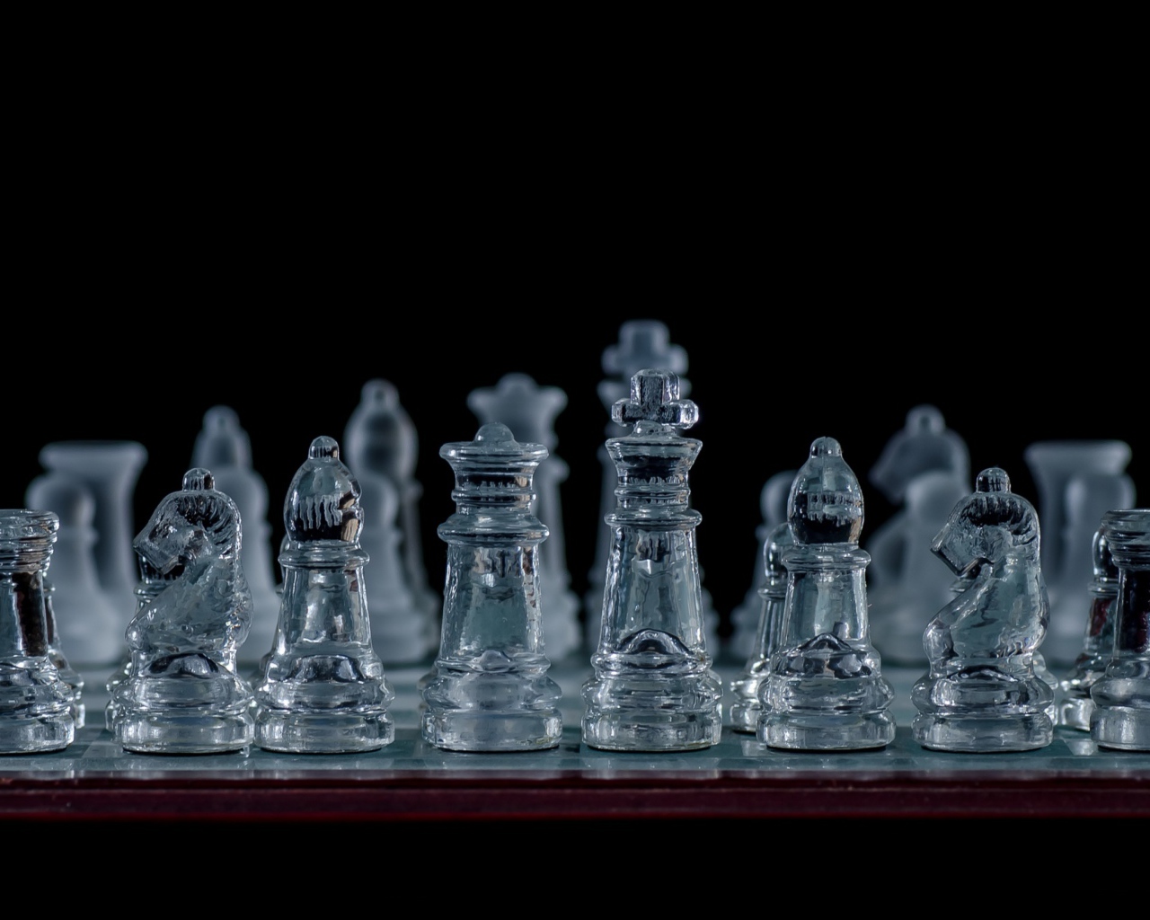 Стеклянные шахматы на доске на черном фоне