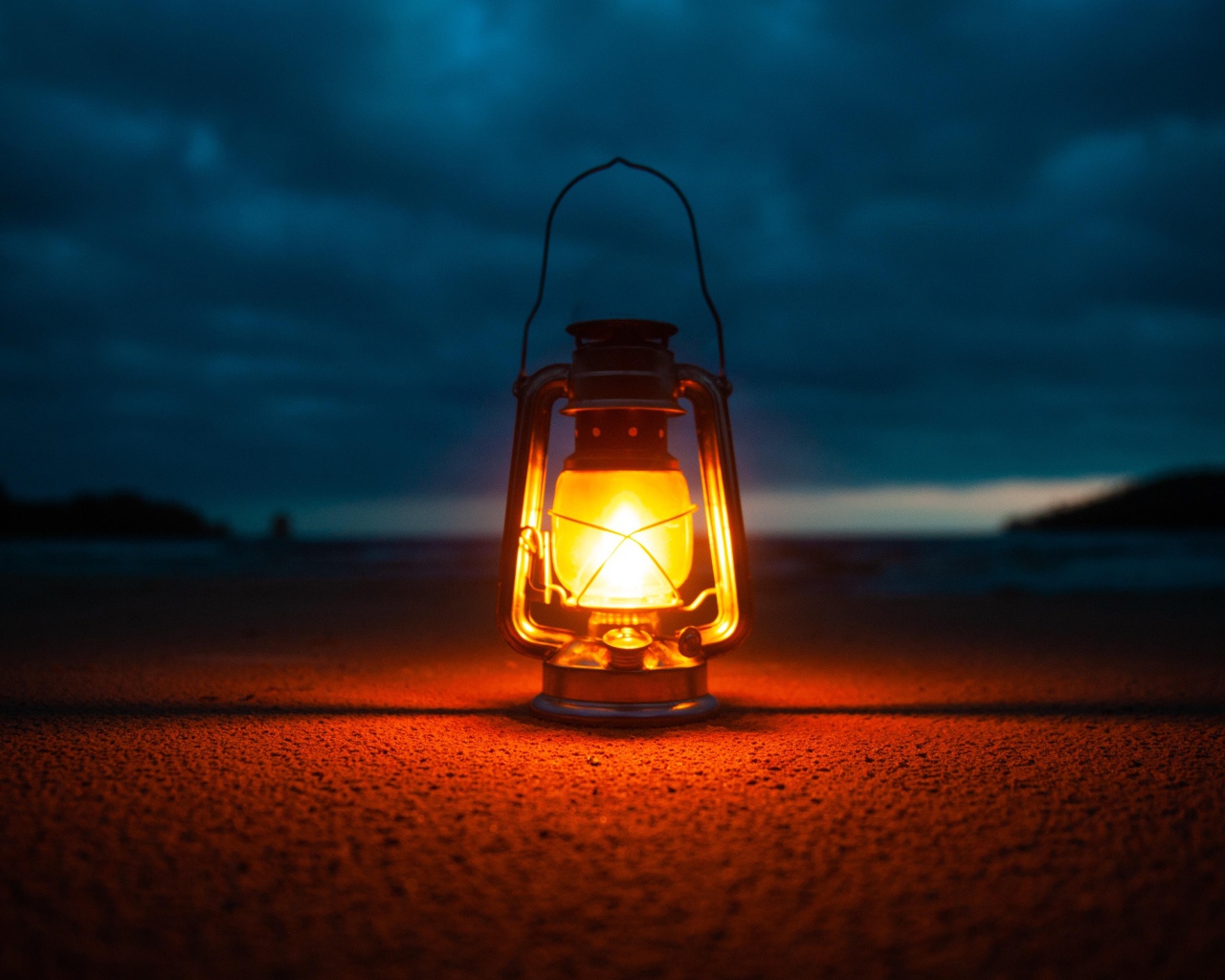 Включенный фонарь стоит на песке у моря 