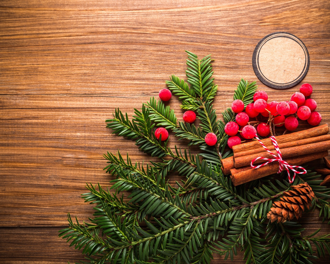 Еловая ветка, корица, ягоды рябины и шишки на деревянном фоне