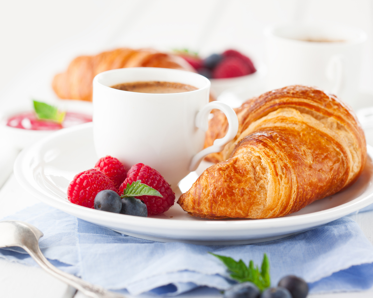 Чашка кофе на тарелке с круассаном и ягодами