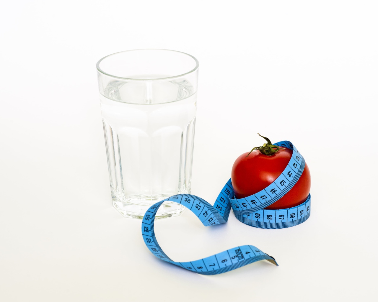 Стакан воды на белом фоне с красным помидором и сантиметром