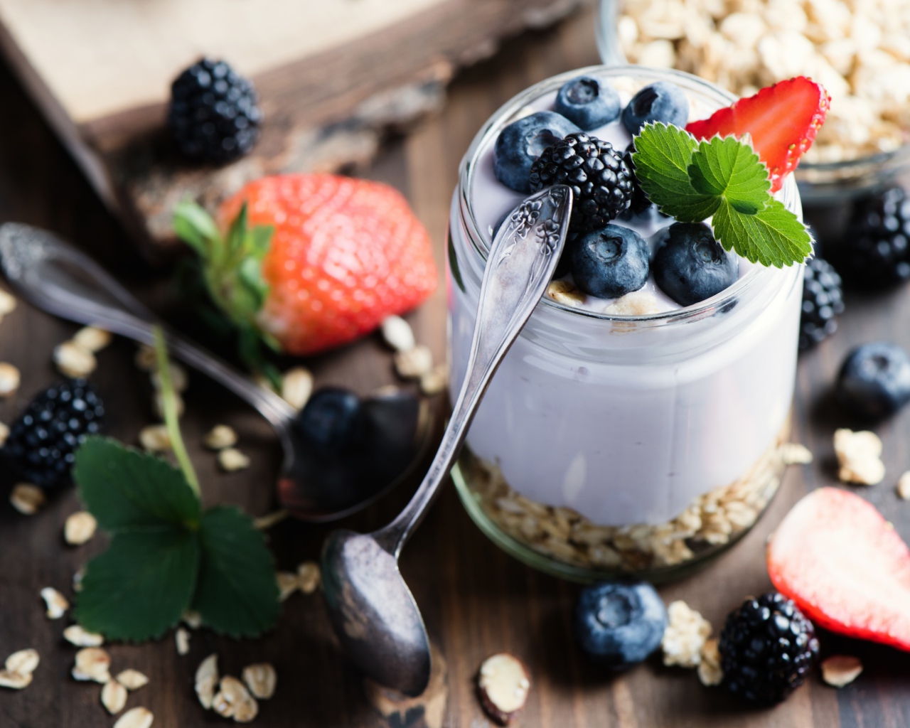 Баночка с мюсли, йогуртом и ягодами на столе с ложками