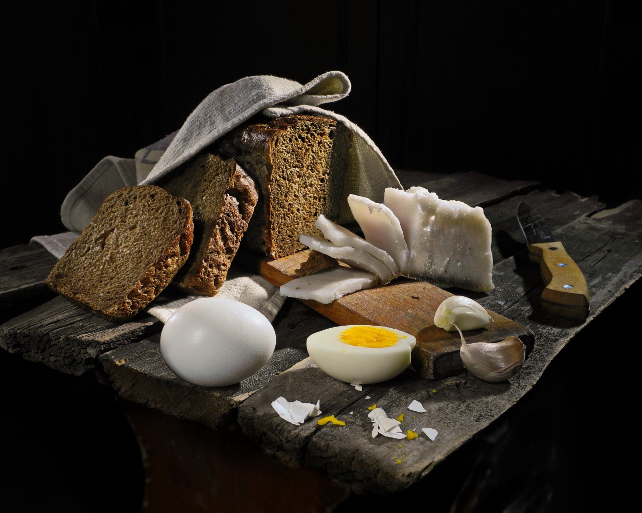 Черный хлеб, вареные яйца, чеснок и сало на деревянном столе