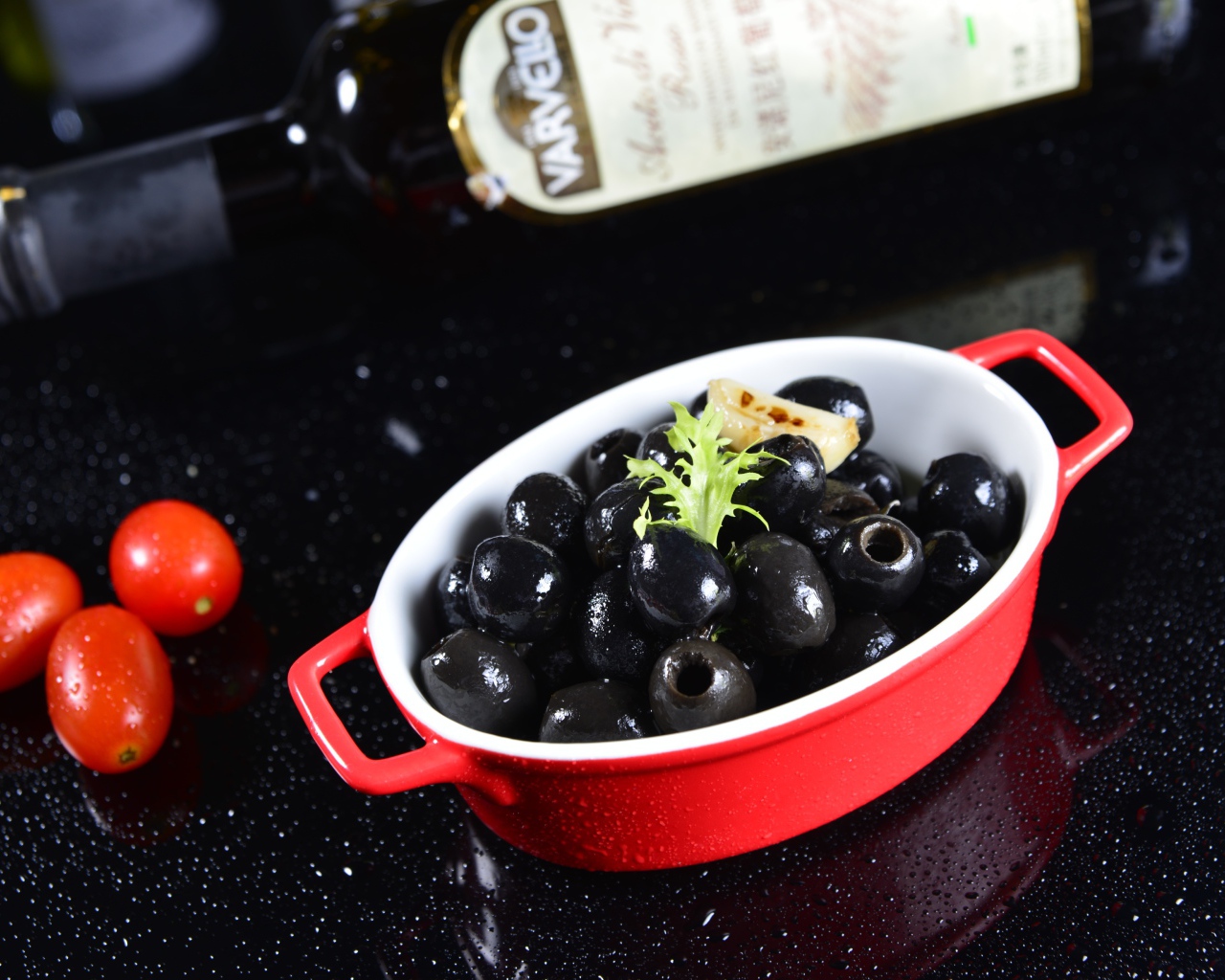 Черные оливки на столе с бутылкой и помидорами
