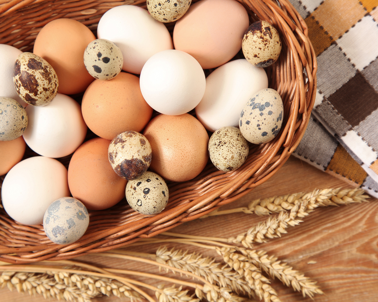 Куриные и перепелиные яйца в корзине на столе с колосками