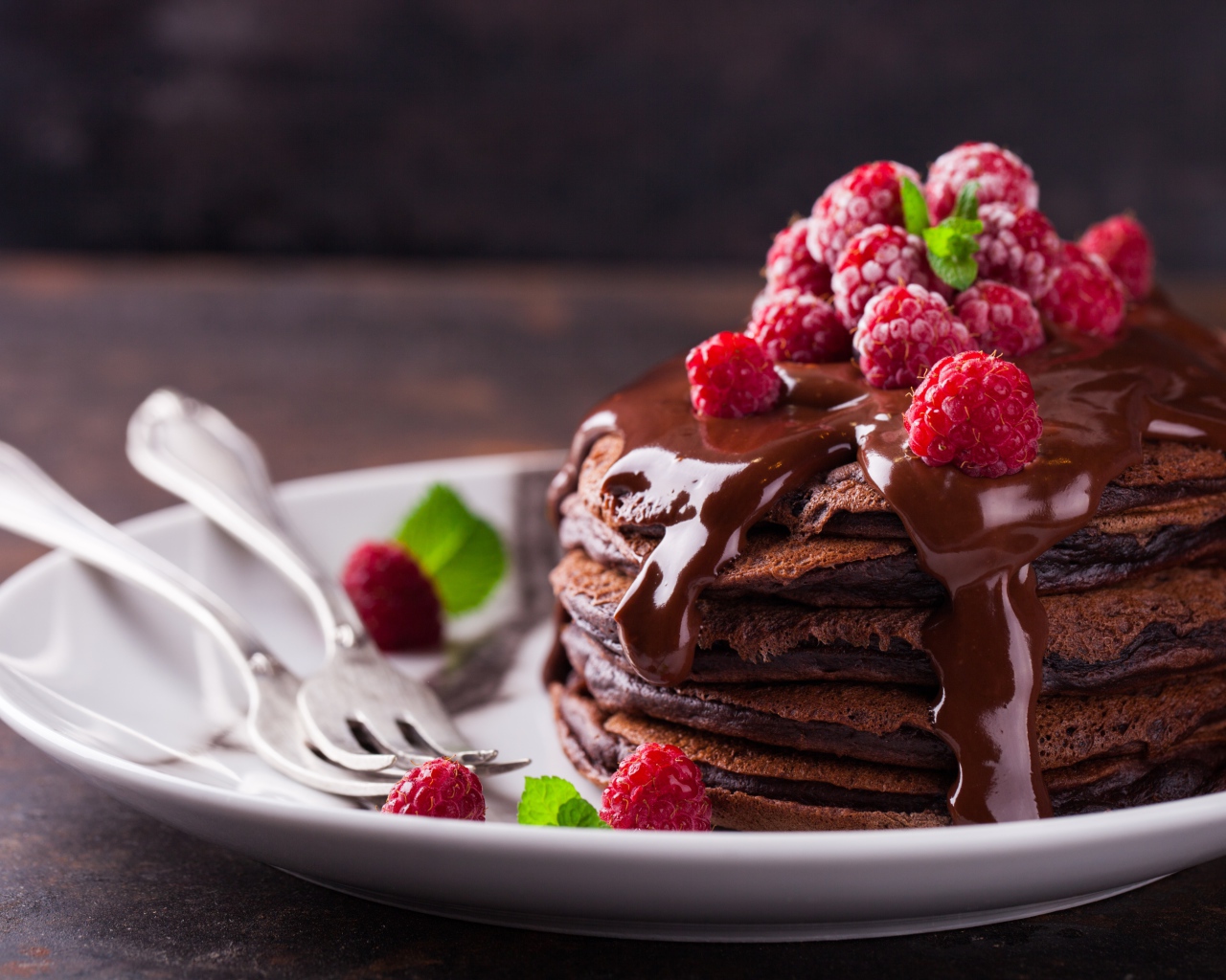 Шоколадные оладьи на тарелке с шоколадом и ягодами малины 