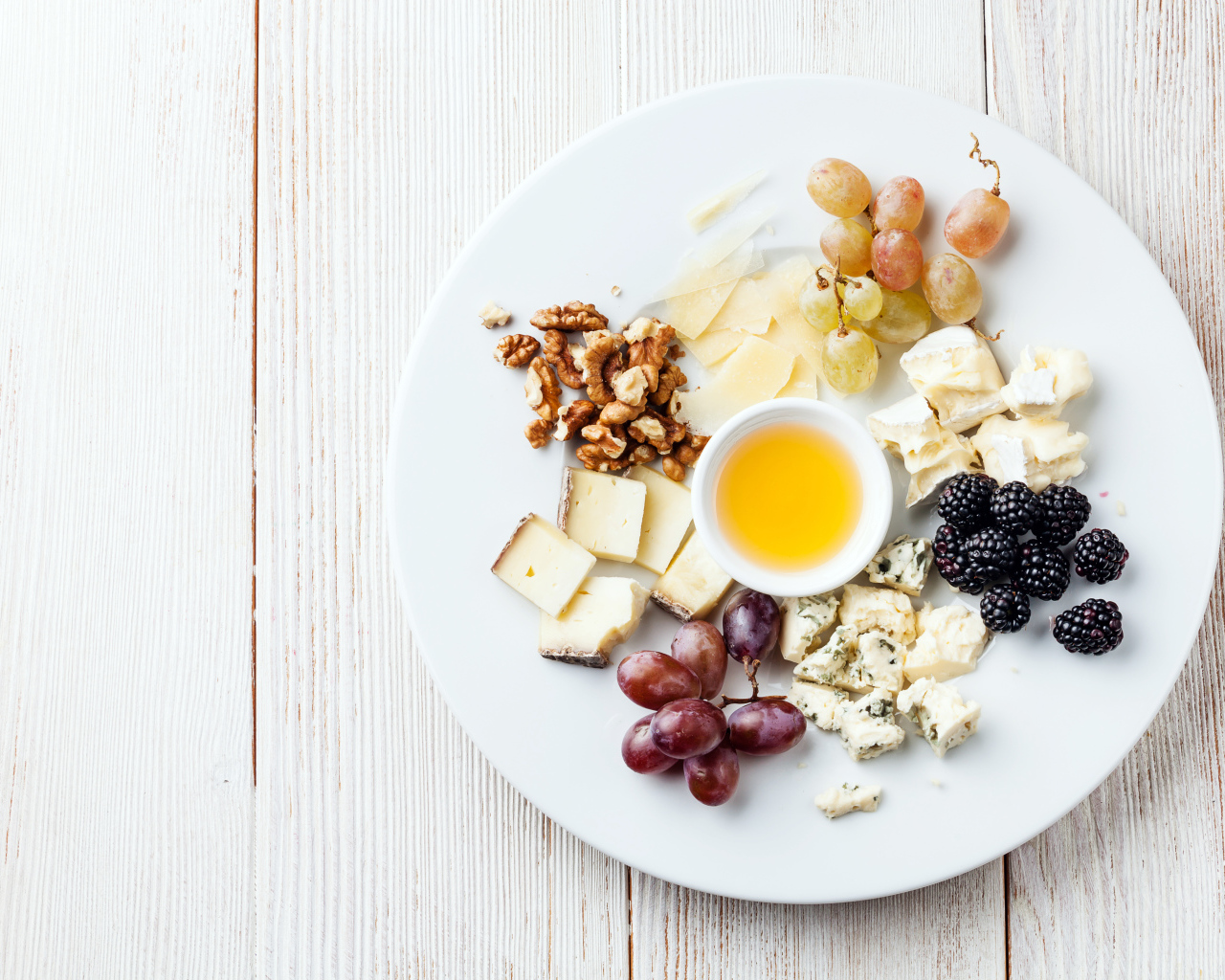 Куски сыра на тарелке с орехами, виноградом, медом и ягодами ежевики