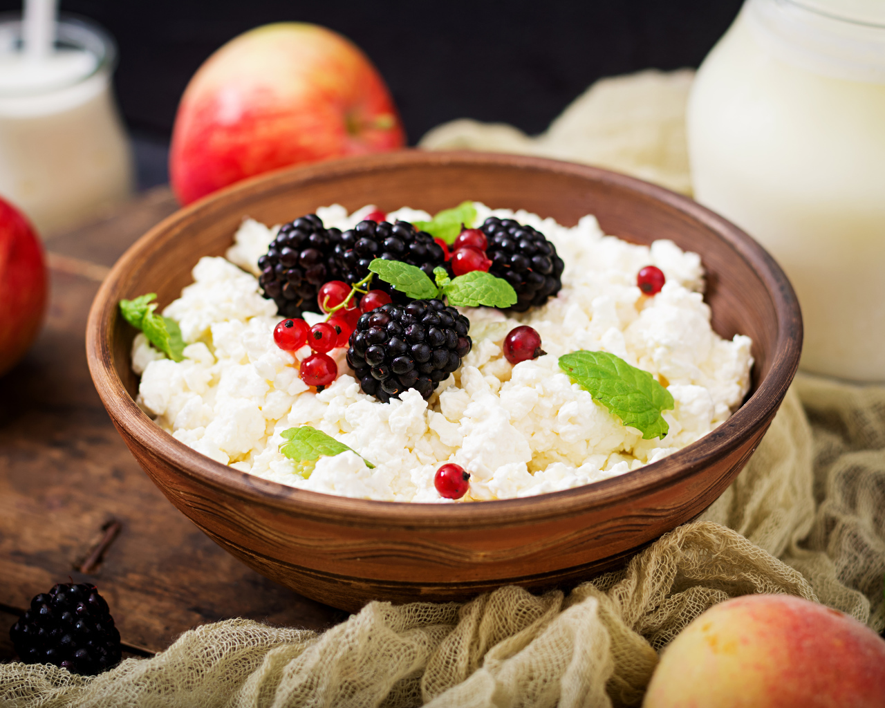 Творог с ягодами в деревянной миске на столе с яблоками