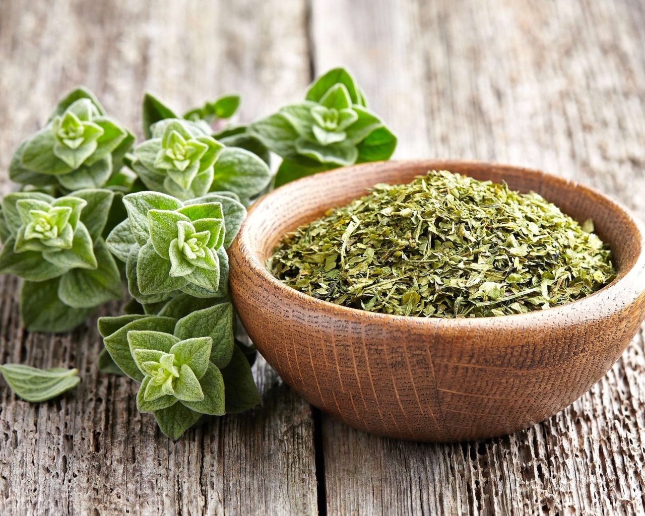 Сухая трава орегано в деревянной миске на столе 