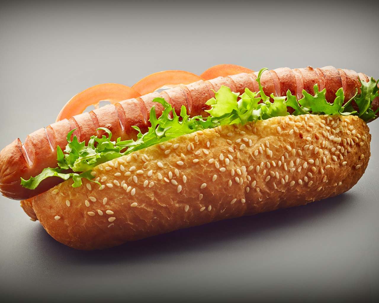 Хотдог с сосиской гриль и листьями салата на сером фоне