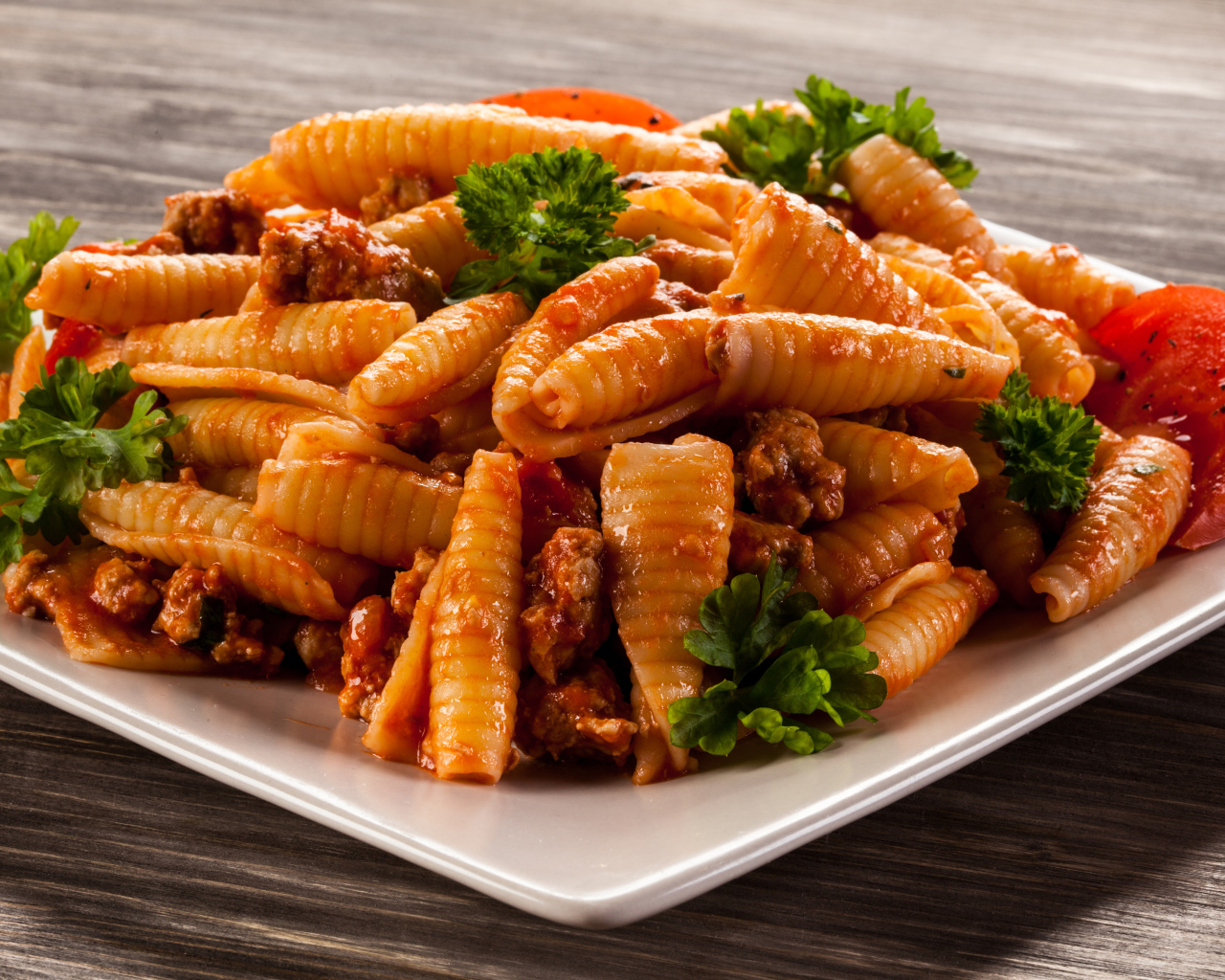 Паста с мясом, петрушкой и помидорами на белой тарелке