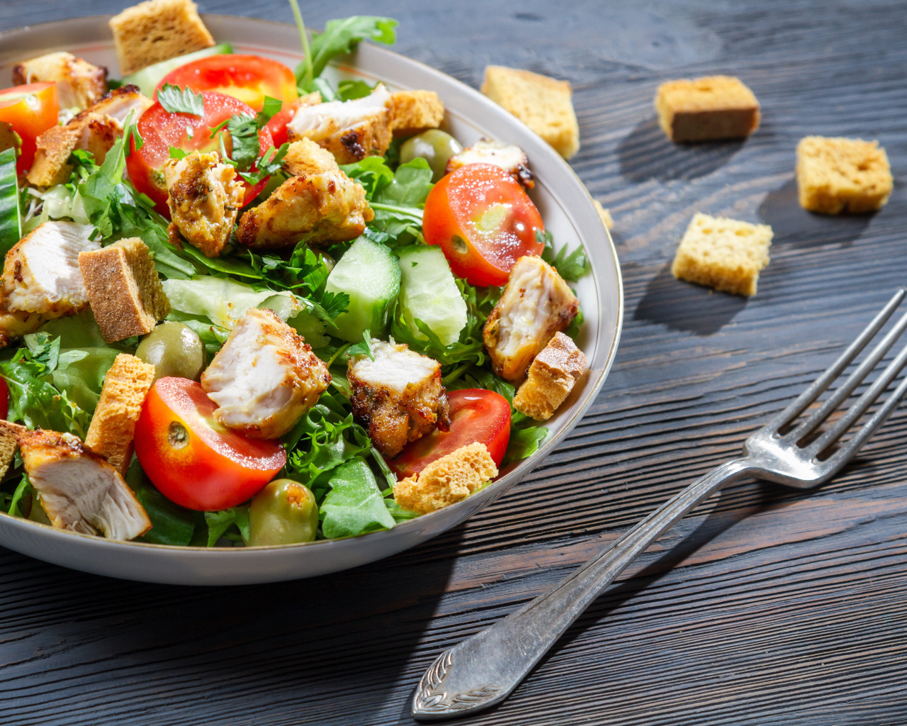 Салат с овощами, сухариками и курицей и на столе с вилкой