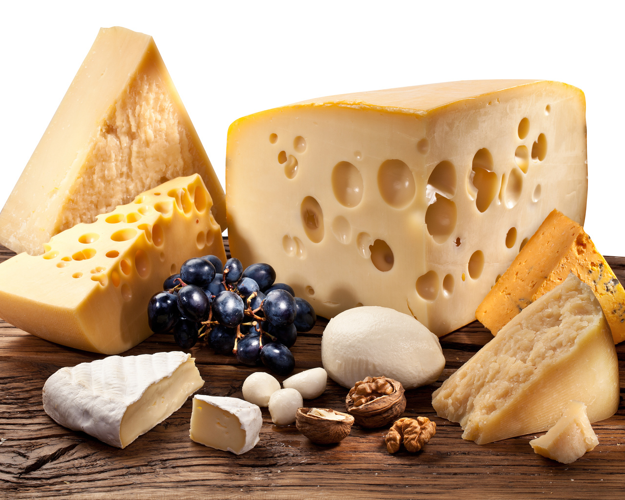 Куски сыра на деревянном столе с виноградом и грецким орехом