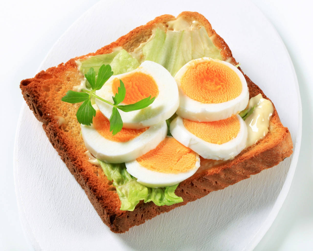 Тост с листом салата и кусочками яйца на белой тарелке 