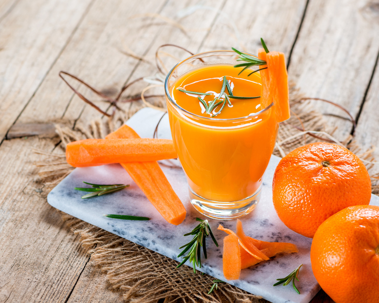 Два апельсина на столе со стаканом морковного сока