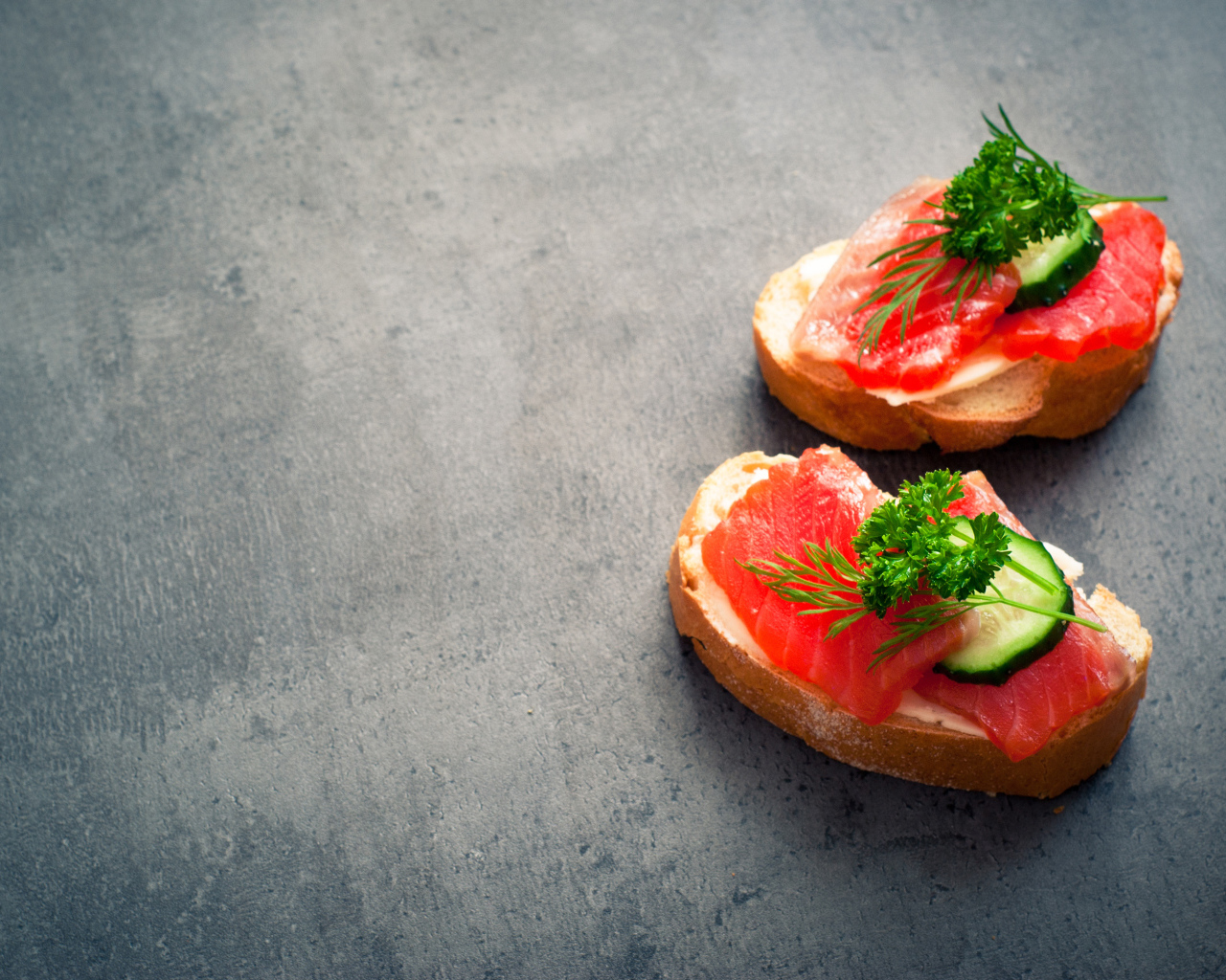 Два бутерброда с красной рыбой, огурцом и зеленью на черном фоне