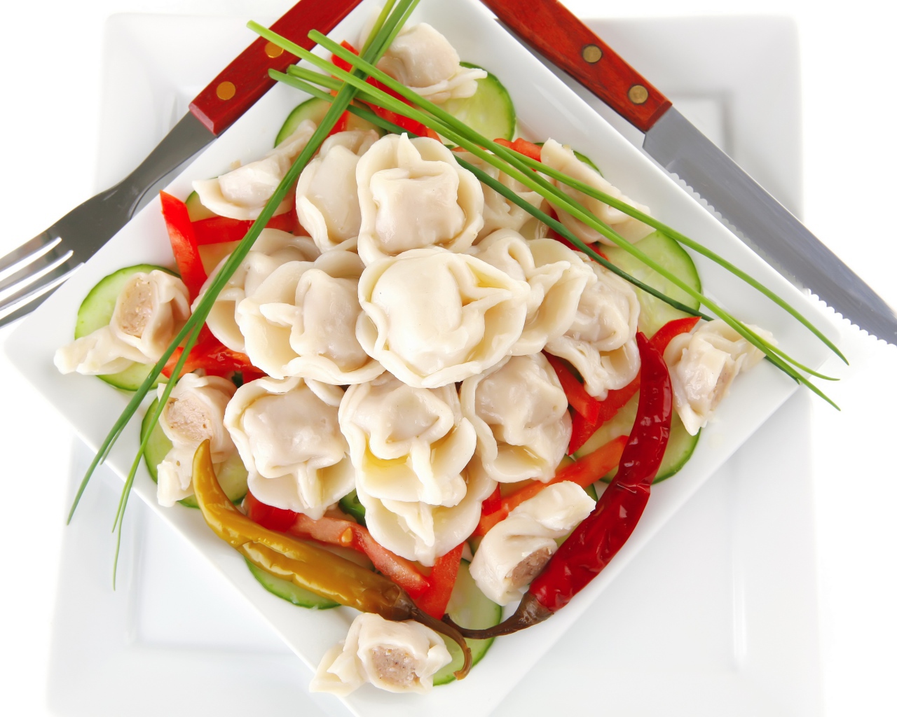 Белая тарелка с пельменями, красным перцем и огурцами