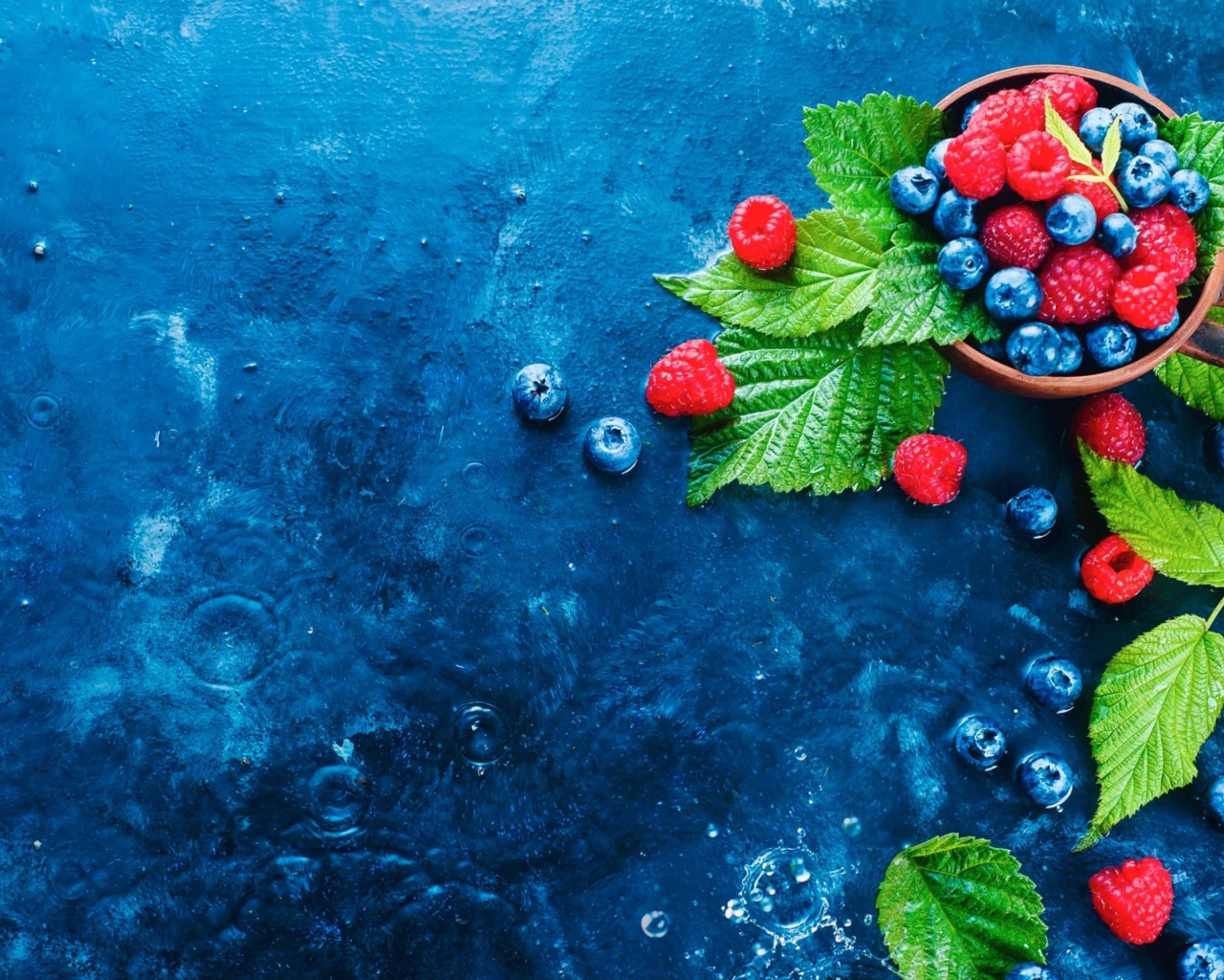 Чашка с ягодами черники и малины на синем столе