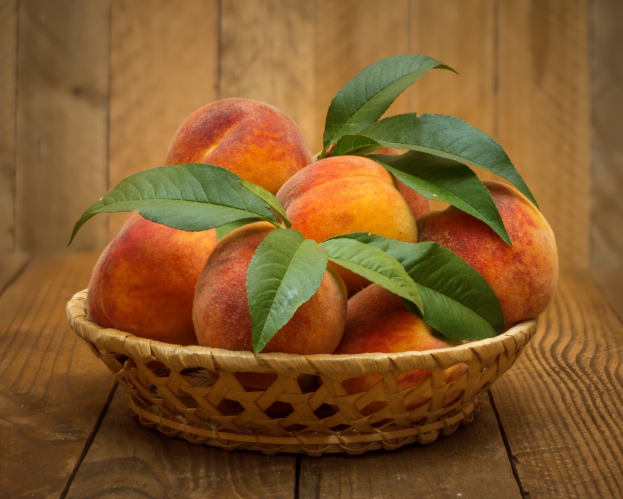 Корзинка персиков с зелеными листьями на столе