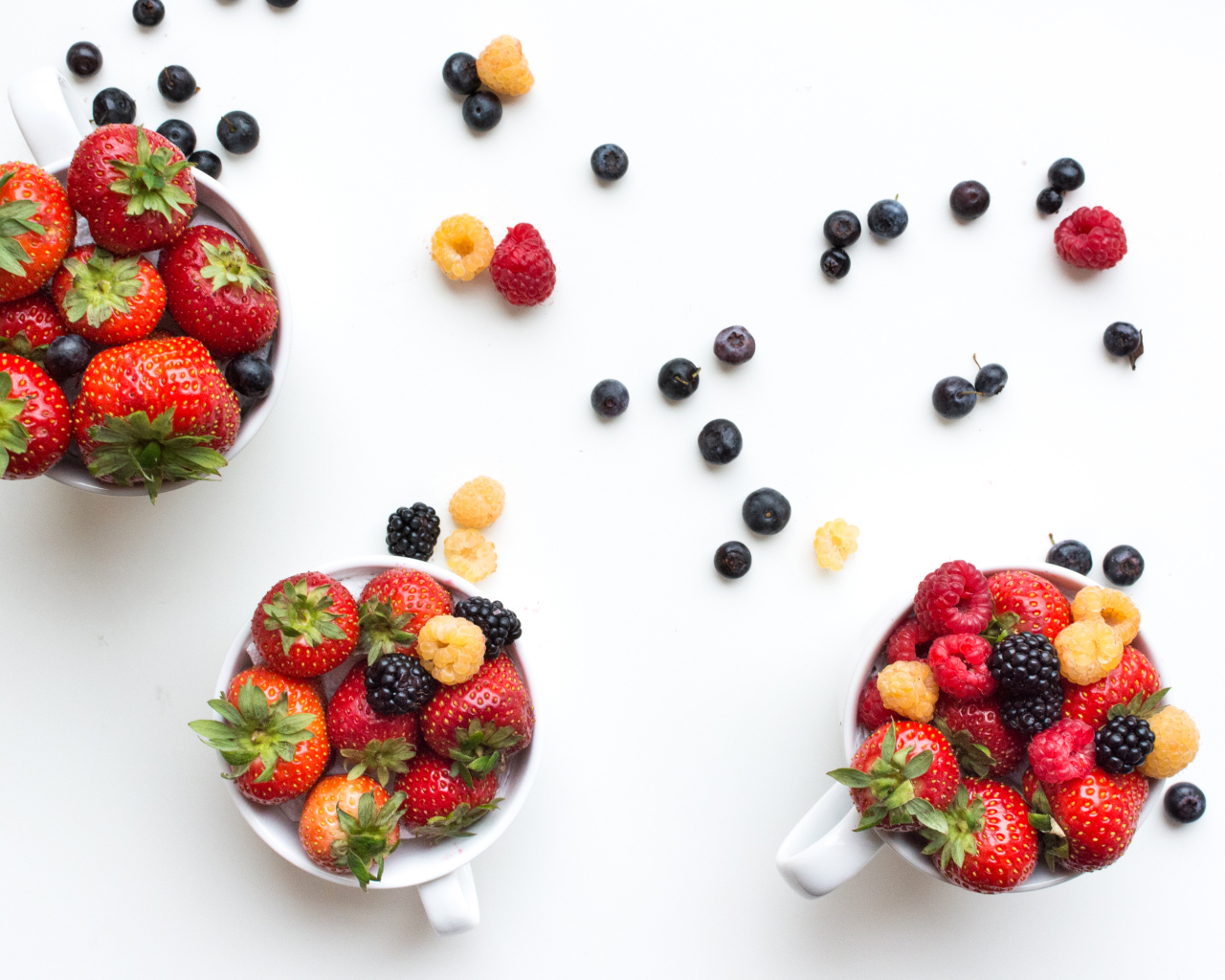 Чашки на столе с ягодами клубники, малины и ежевики 