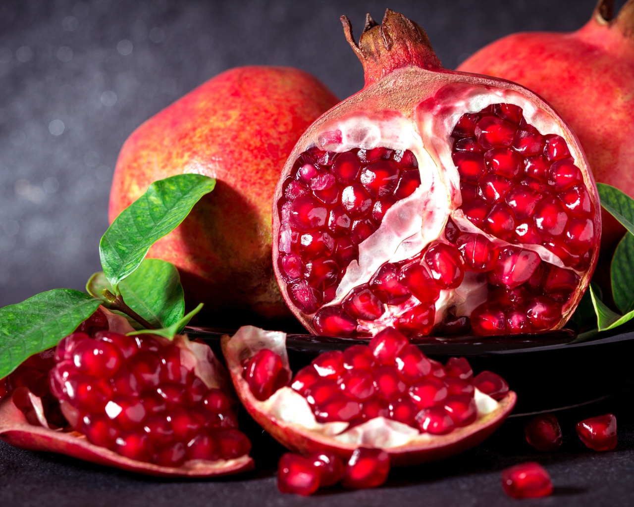 Красные гранаты с зернами и зелеными листьями на сером фоне