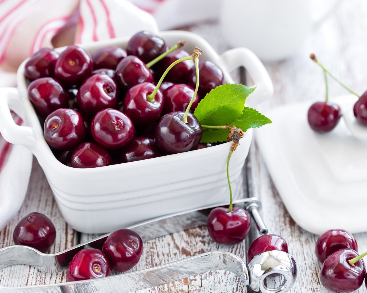 Красные спелые вишни в белой тарелке на столе