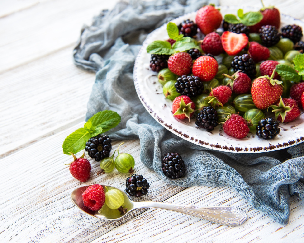 Спелые ягоды крыжовника, ежевики, малины и клубники на тарелке