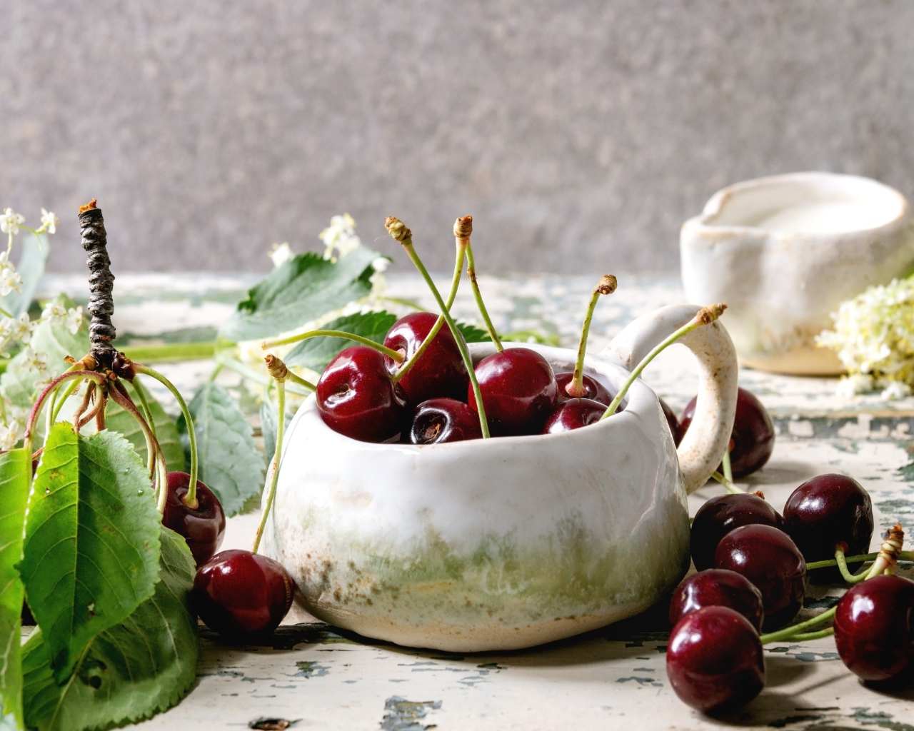 Спелые красные черешни на столе в белом чайнике