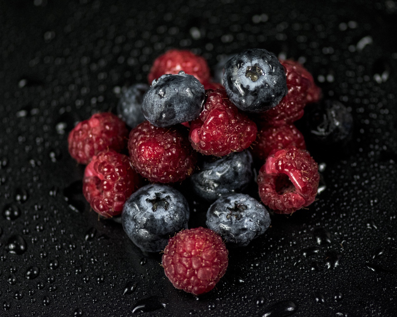 Мокрые ягоды черники и малины на черном фоне