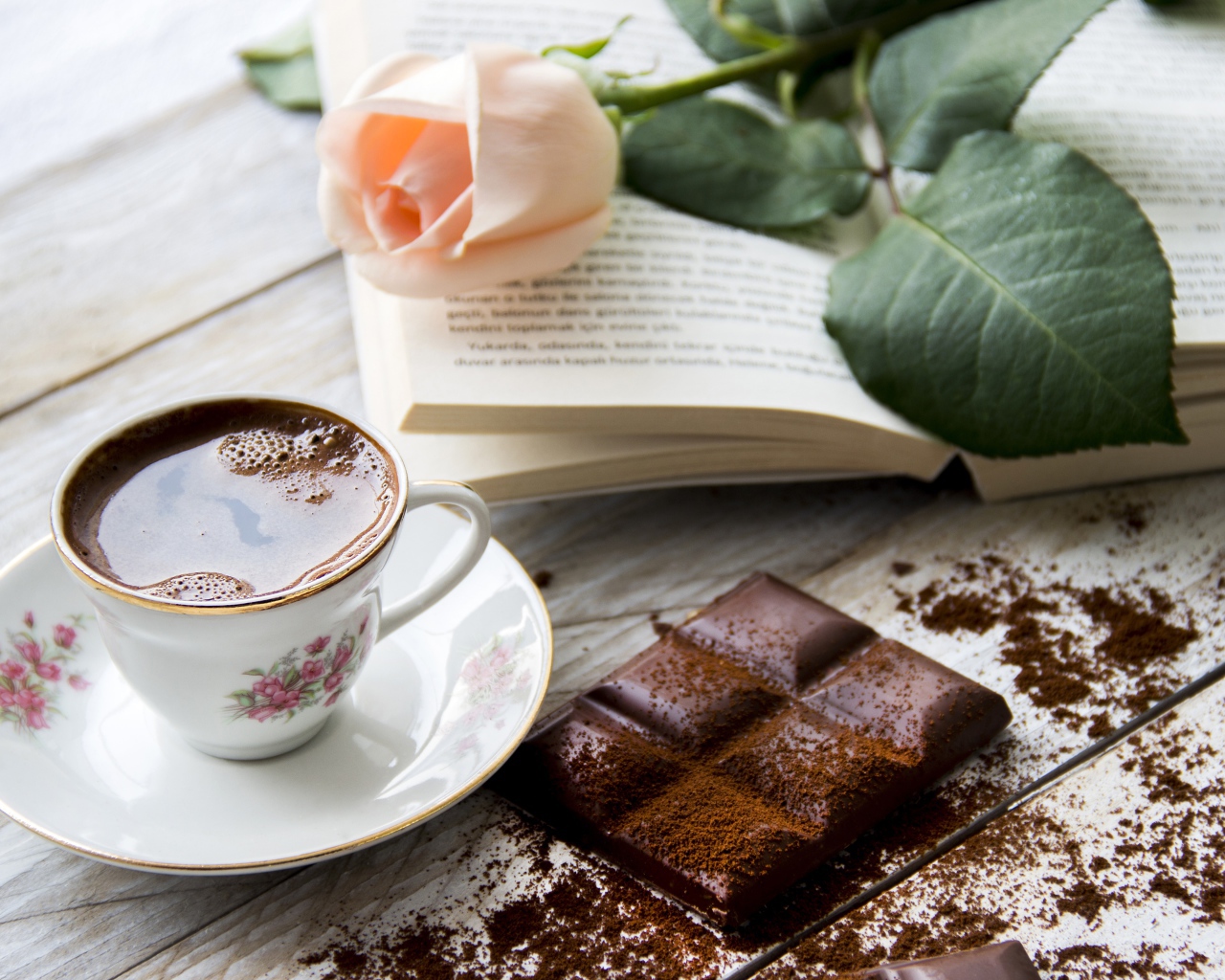 Чашка кофе на столе с шоколадом, книгой и розой